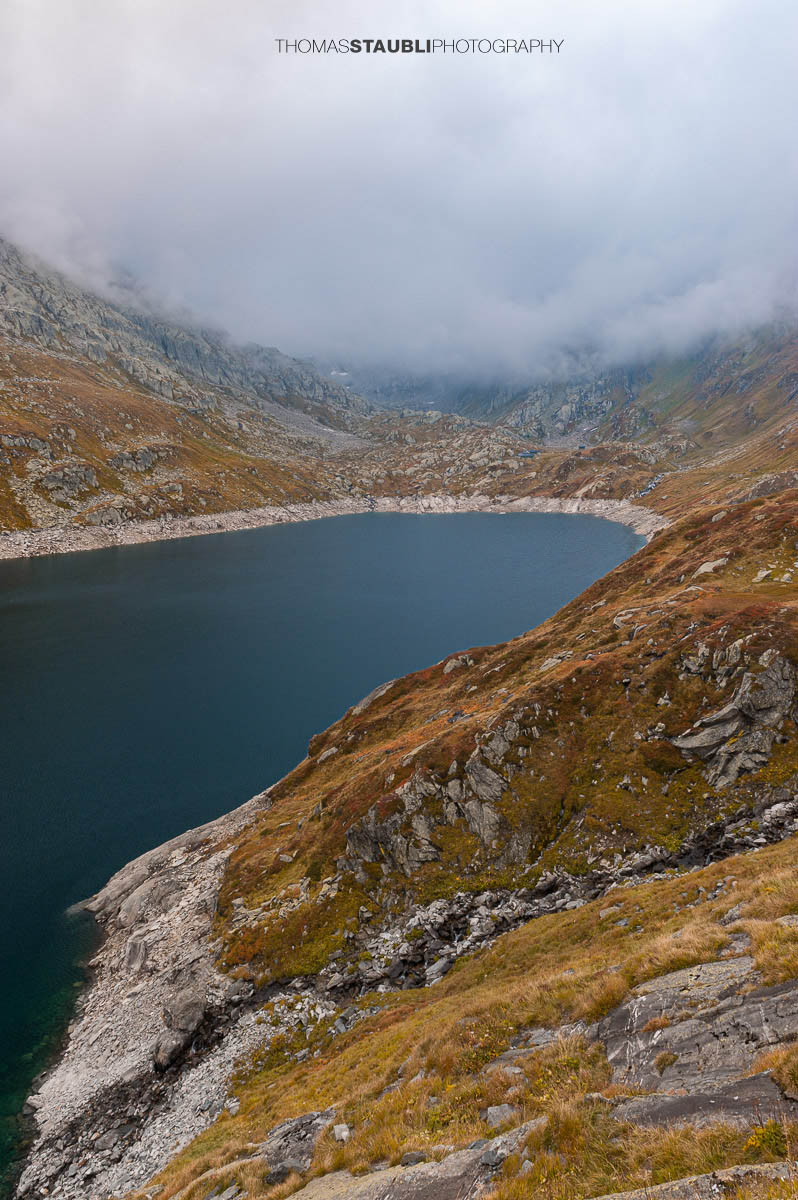 Lago di Lucendro am Gotthardpass, umgeben von felsigen Hängen und aufziehenden Wolken.