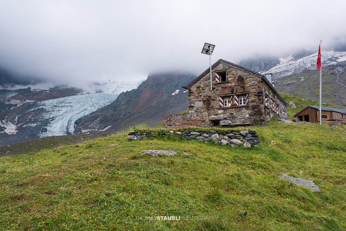 Fridolinshütte im Kanton Glarus in der Morgendämmerung, dahinter der Gletscher Bifertenfirn unter steilen Felswänden.