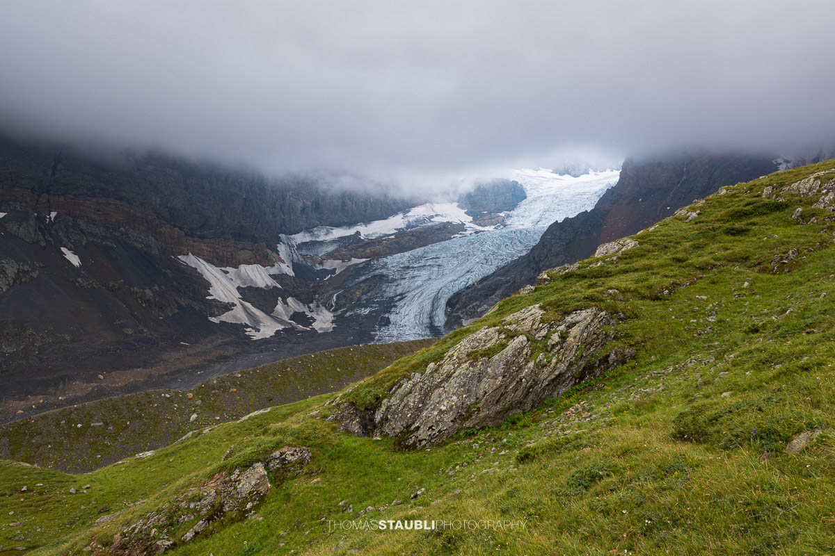 Blick auf den Bifertenfirn im Jahr 2013 im Kanton Glarus, teilweise von tief hängenden Wolken umgeben, mit sichtbarem Gletscherstrom, Schuttflächen und steilen Felswänden in alpiner Hochgebirgslandschaft.