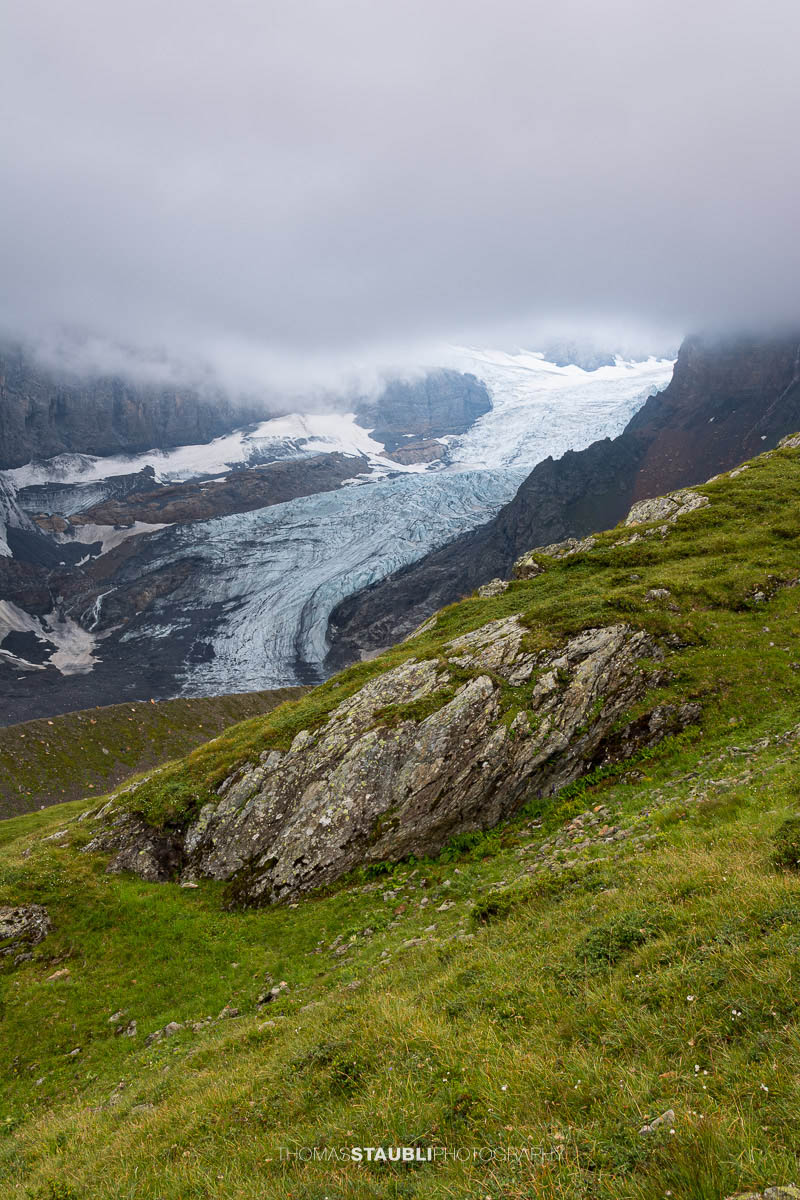 Blick auf den Bifertenfirn im Jahr 2013 im Kanton Glarus, teilweise von tief hängenden Wolken umgeben, mit sichtbarem Gletscherstrom, Schuttflächen und steilen Felswänden in alpiner Hochgebirgslandschaft.