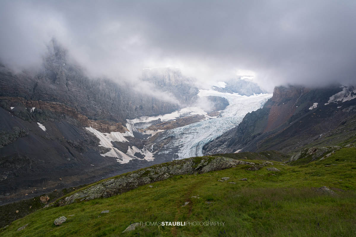 Blick auf den Bifertenfirn im Jahr 2013 im Kanton Glarus, teilweise von tief hängenden Wolken umgeben, mit sichtbarem Gletscherstrom, Schuttflächen und steilen Felswänden in alpiner Hochgebirgslandschaft.