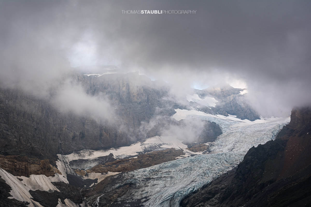 Blick auf den Bifertenfirn im Jahr 2013 im Kanton Glarus, teilweise von tief hängenden Wolken umgeben, mit sichtbarem Gletscherstrom, Schuttflächen und steilen Felswänden in alpiner Hochgebirgslandschaft.
