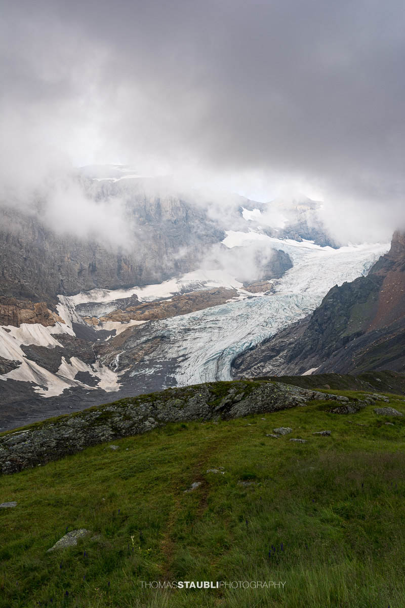 Blick auf den Bifertenfirn im Jahr 2013 im Kanton Glarus, teilweise von tief hängenden Wolken umgeben, mit sichtbarem Gletscherstrom, Schuttflächen und steilen Felswänden in alpiner Hochgebirgslandschaft.
