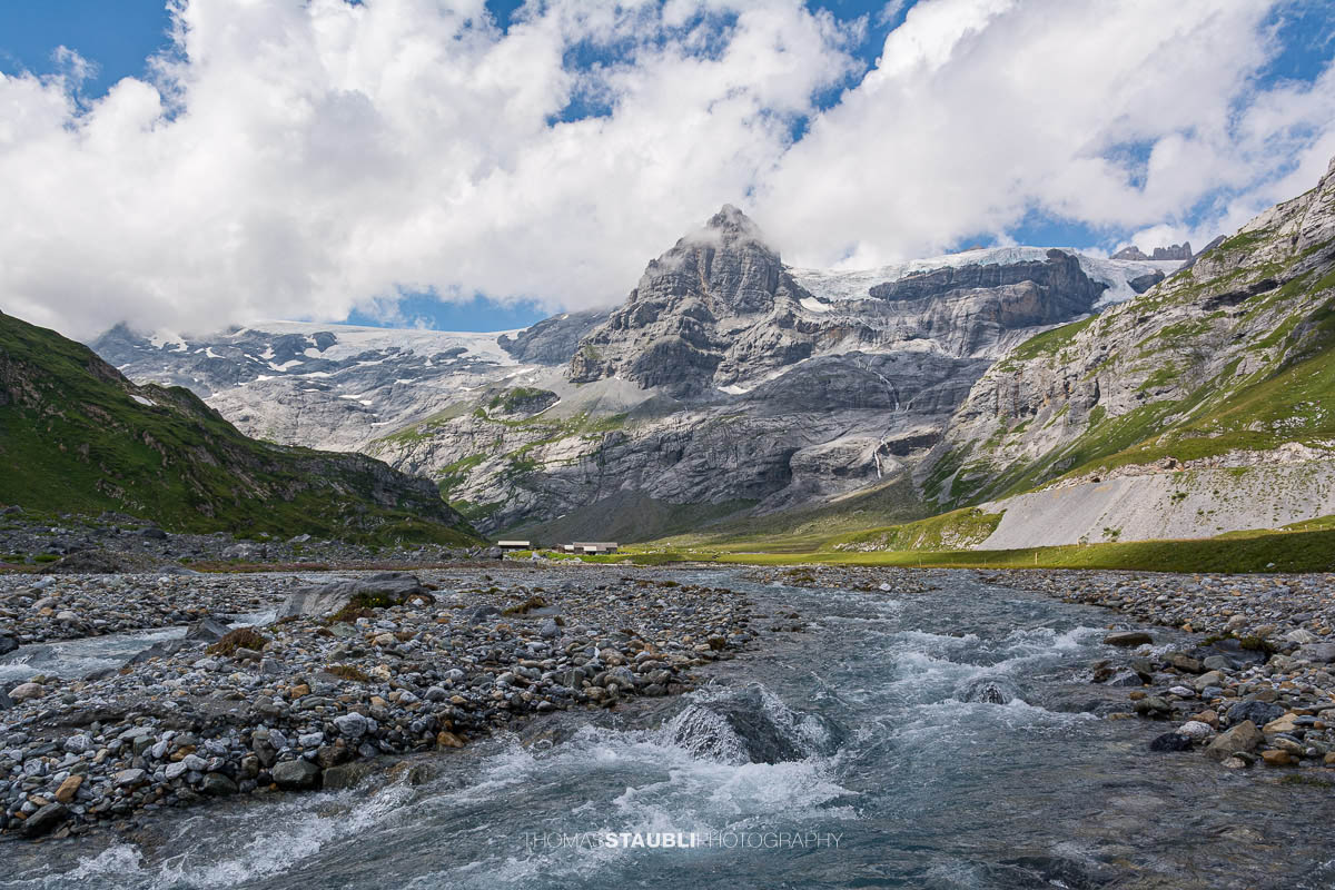 Oberstafelbach auf der Alp Ober Sand im Kanton Glarus; im Hintergrund in der Bildmitte der Spitzalpelistock, rechts davon der Claridenfirn, umgeben von Geröllflächen, alpiner Ebene und steilen Felswänden.