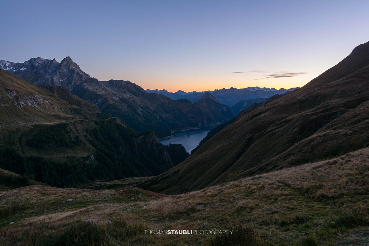 Abenddämmerung oberhalb der Capanna Motterascio mit Blick über alpine Hänge zum Lago di Luzzone und den umliegenden Bergketten der Greina-Region im Tessin.