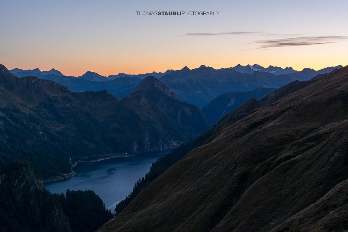 Abenddämmerung oberhalb der Capanna Motterascio mit Blick über alpine Hänge zum Lago di Luzzone und den umliegenden Bergketten der Greina-Region im Tessin.