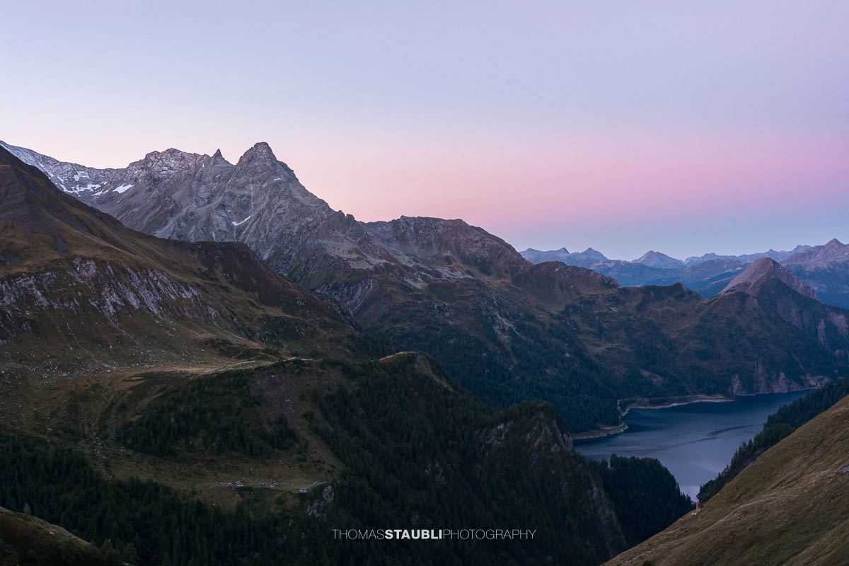 Morgendämmerung oberhalb der Capanna Motterascio mit Blick über alpine Hänge zum Lago di Luzzone und den umliegenden Bergketten der Greina-Region im Tessin.