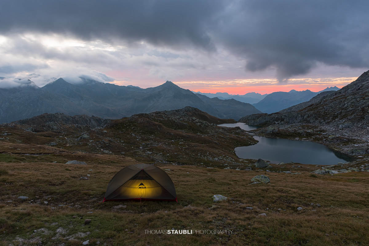 Morgenrot über den Laghi della Valletta: kleine Hochgebirgsseen in felsiger Landschaft, dunkle Wolken und roter Horizont über den Tessiner Alpen.