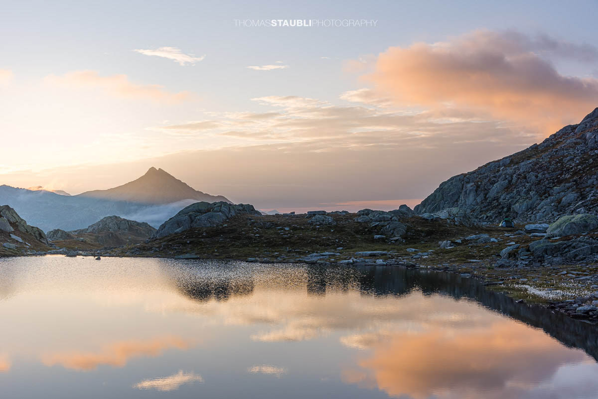 Morgenstimmung an den Laghi della Valletta: ruhiger Bergsee mit Spiegelung von Himmel und Wolken, sanftes Morgenlicht über einer kargen Hochalpenlandschaft im Tessin.