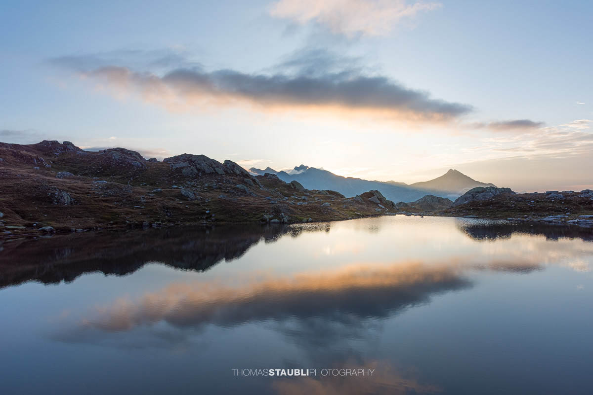 Morgenstimmung an den Laghi della Valletta: ruhiger Bergsee mit Spiegelung von Himmel und Wolken, sanftes Morgenlicht über einer kargen Hochalpenlandschaft im Tessin.