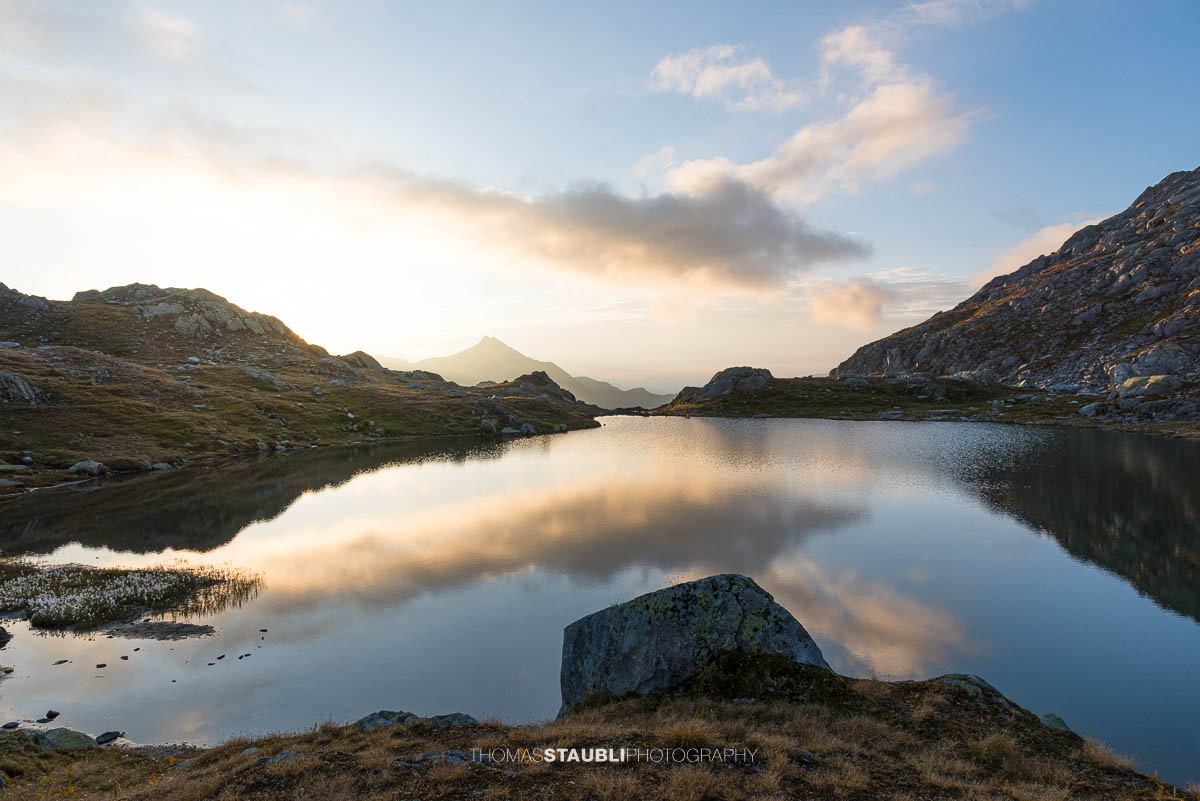 Morgenstimmung an den Laghi della Valletta: ruhiger Bergsee mit Spiegelung von Himmel und Wolken, sanftes Morgenlicht über einer kargen Hochalpenlandschaft im Tessin.
