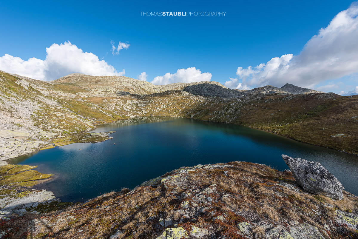 Blick auf die Laghi della Valletta: dunkelblauer Hochgebirgssee in karger Felslandschaft, links im Hintergrund der Übergang am Passo d'Orsirora unter weitem Himmel.