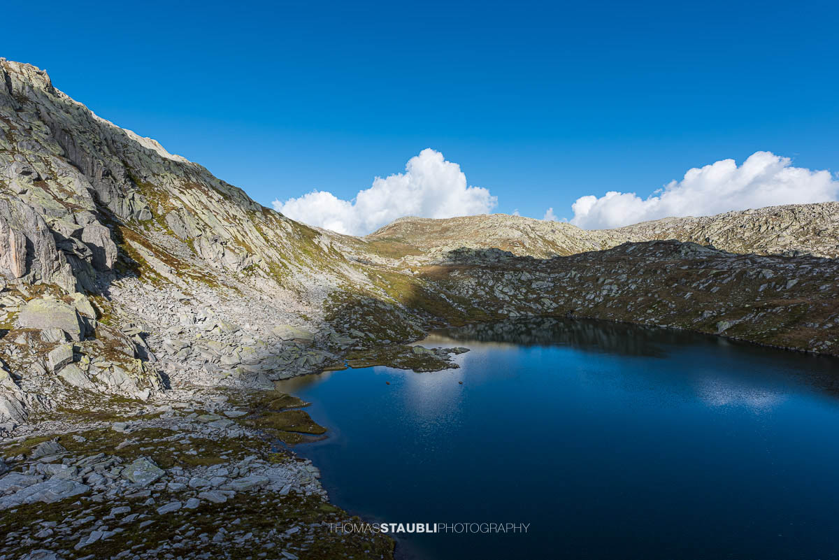 Blick auf die Laghi della Valletta: dunkelblauer Hochgebirgssee in karger Felslandschaft, im Hintergrund der Übergang am Passo d'Orsirora unter weitem Himmel.