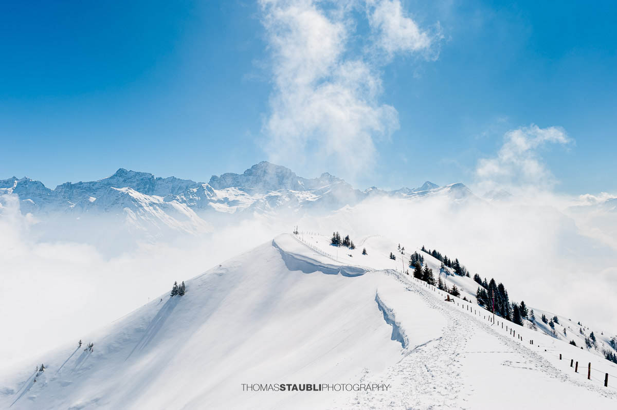 Schneeschuhspur auf einem verschneiten Grat nahe der Hüenderegg mit weiter Sicht auf die Urner Alpen.
