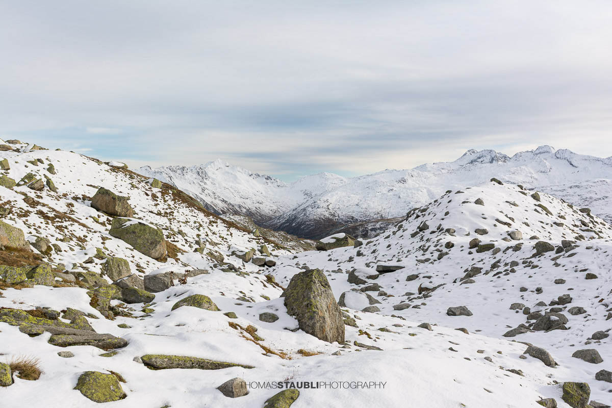 Blick zum Pizzo Lucendro im Urserental, verschneite Gipfel und herbstlich gefärbte Hänge im Übergang zum Winter.