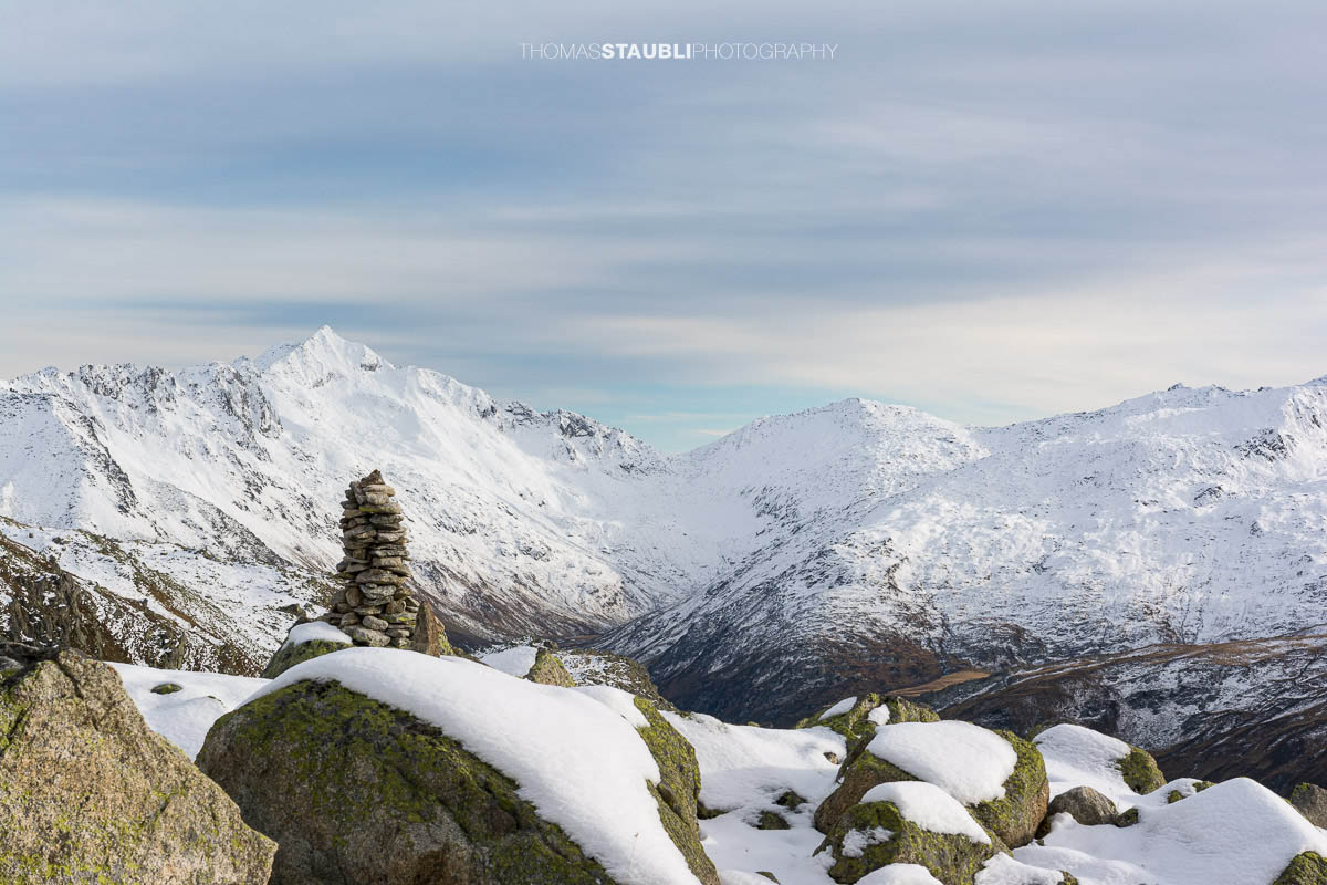Blick zum Pizzo Lucendro im Urserental, verschneite Gipfel und herbstlich gefärbte Hänge im Übergang zum Winter.
