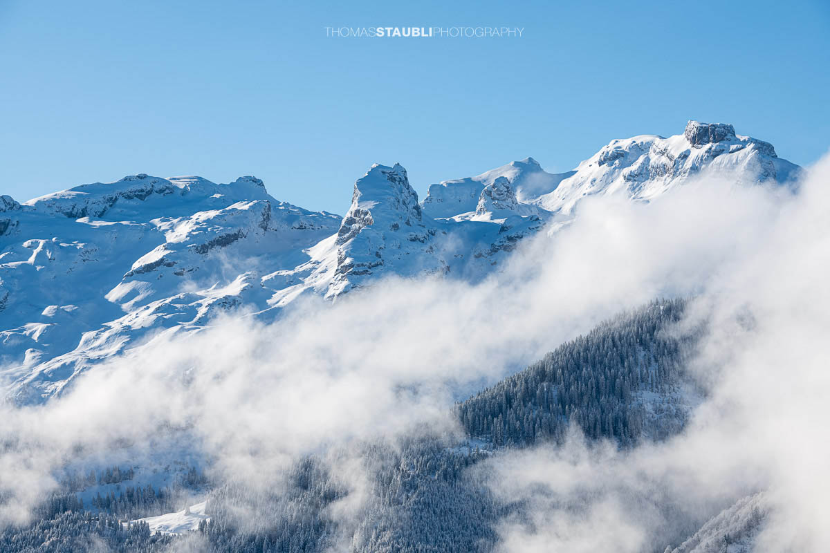 Blick zum Gross Achslenstock im Kanton Schwyz, verschneite Bergflanken über aufziehendem Nebel und winterlichem Wald.