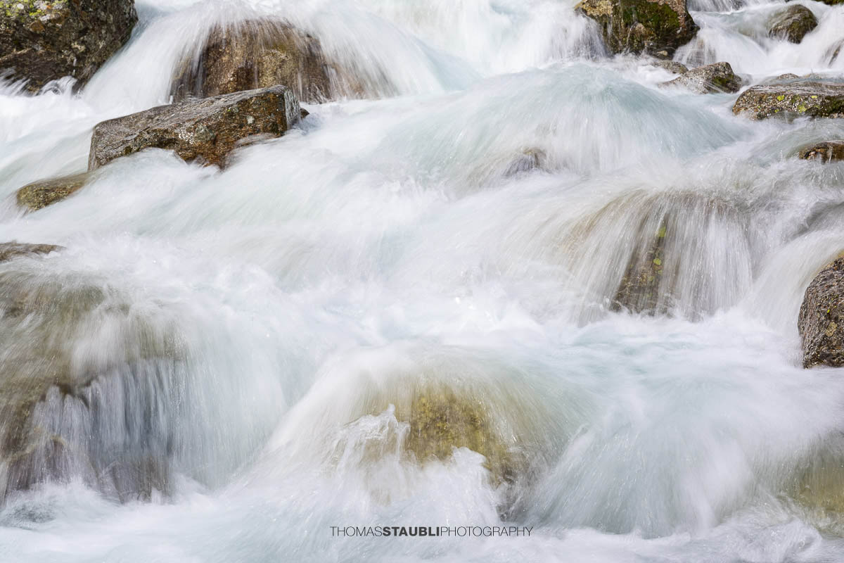 Dammareuss im Göschenertal im Kanton Uri, klarer Gebirgsbach zwischen Felsen und alpiner Vegetation.