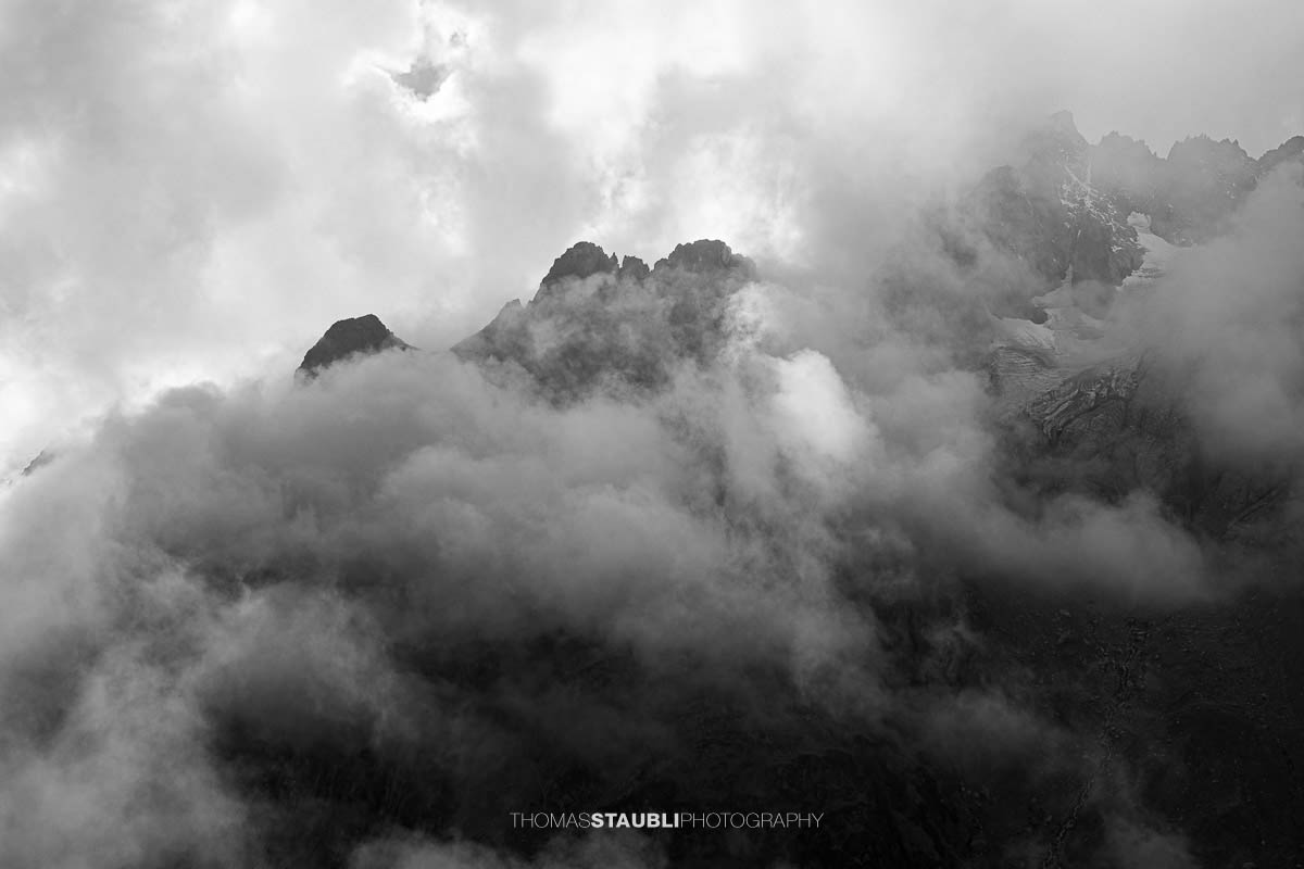 Blick zum Guferstock und Sustenlochspitz in den Urner Alpen, schroffe Berggipfel von dichtem Nebel und Wolken umhüllt.