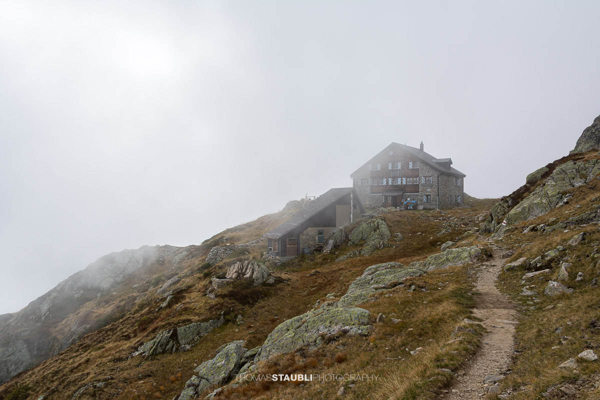 Sustlihütte im Meiental, umgeben von Felsen und alpiner Landschaft, bei nebligem Wetter mit Wanderweg im Vordergrund.