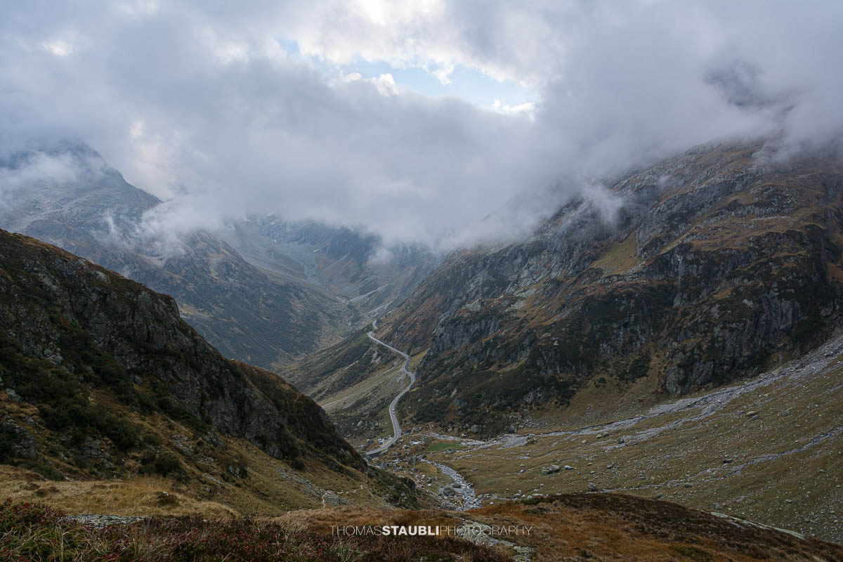 Blick hinunter zur Sustenpassstrasse im Meiental, kurvige Passstrasse zwischen steilen Berghängen und unter tiefhängenden Wolken.