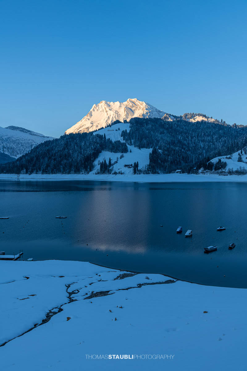 Morgenstimmung am Wägitalersee im Kanton Schwyz mit spiegelnder Wasseroberfläche und dem Fluebrig im ersten Sonnenlicht im Hintergrund.