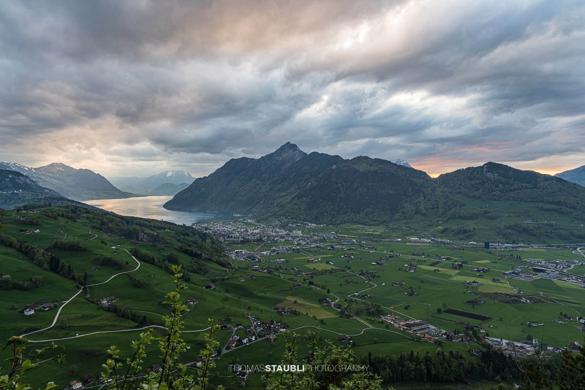 Abendstimmung über dem Talkessel von Schwyz mit Vierwaldstättersee und umliegenden Bergen unter dramatischem Himmel.