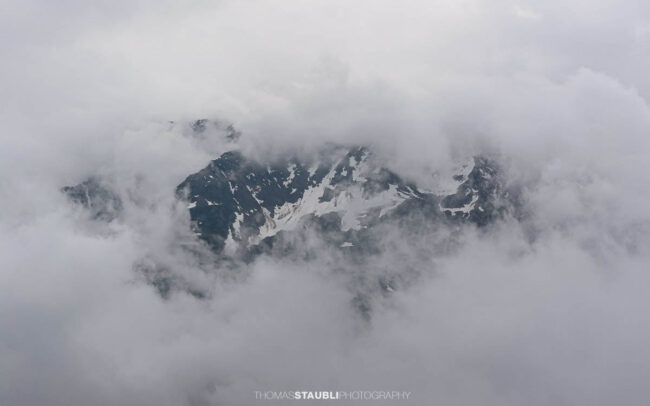 Teilweise von Wolken verhüllter Alpengipfel mit Schneefeldern in den Schweizer Alpen.