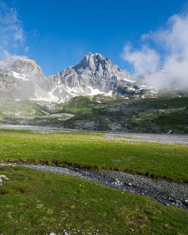 Blick zum Gross Windgällen im Maderanertal mit alpinen Wiesen, Schmelzwasserbach und aufziehenden Nebelschwaden.