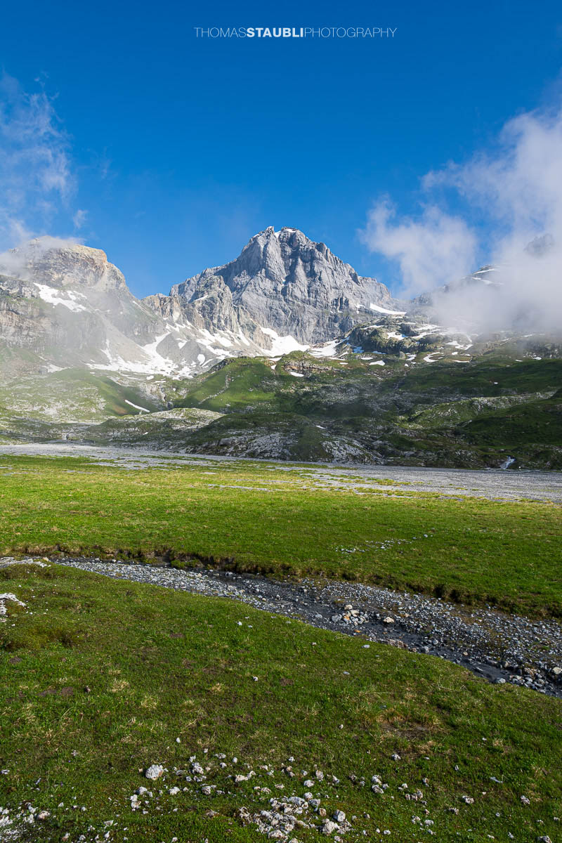Blick zum Gross Windgällen im Maderanertal mit alpinen Wiesen, Schmelzwasserbach und aufziehenden Nebelschwaden.