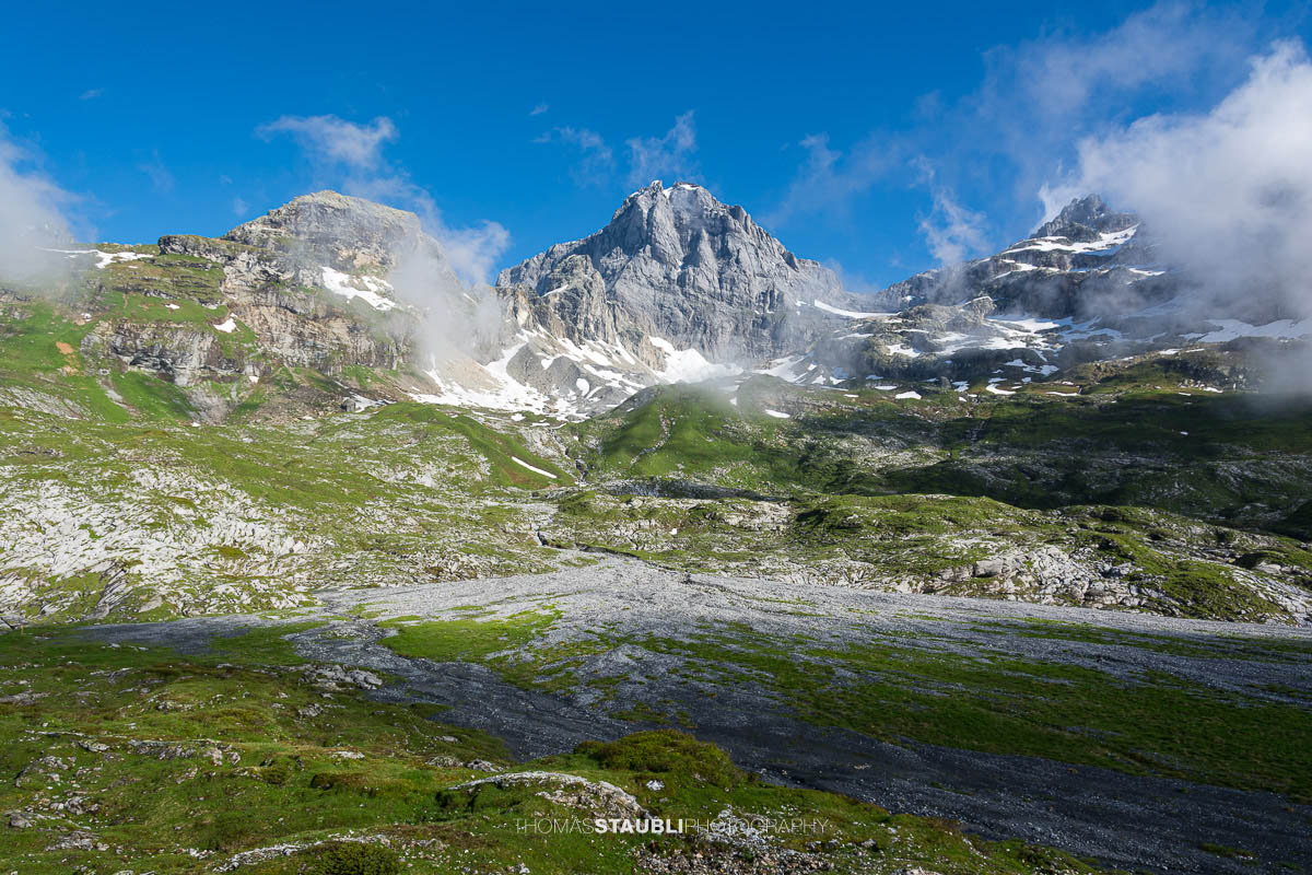 Blick zum Gross Windgällen im Maderanertal mit alpinen Wiesen, Schmelzwasserbach und aufziehenden Nebelschwaden.