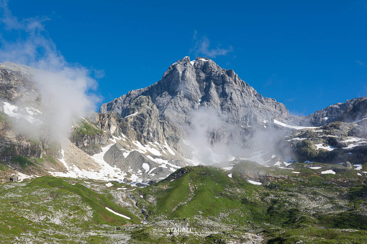 Blick zum Gross Windgällen im Maderanertal mit alpinen Wiesen, Schmelzwasserbach und aufziehenden Nebelschwaden.