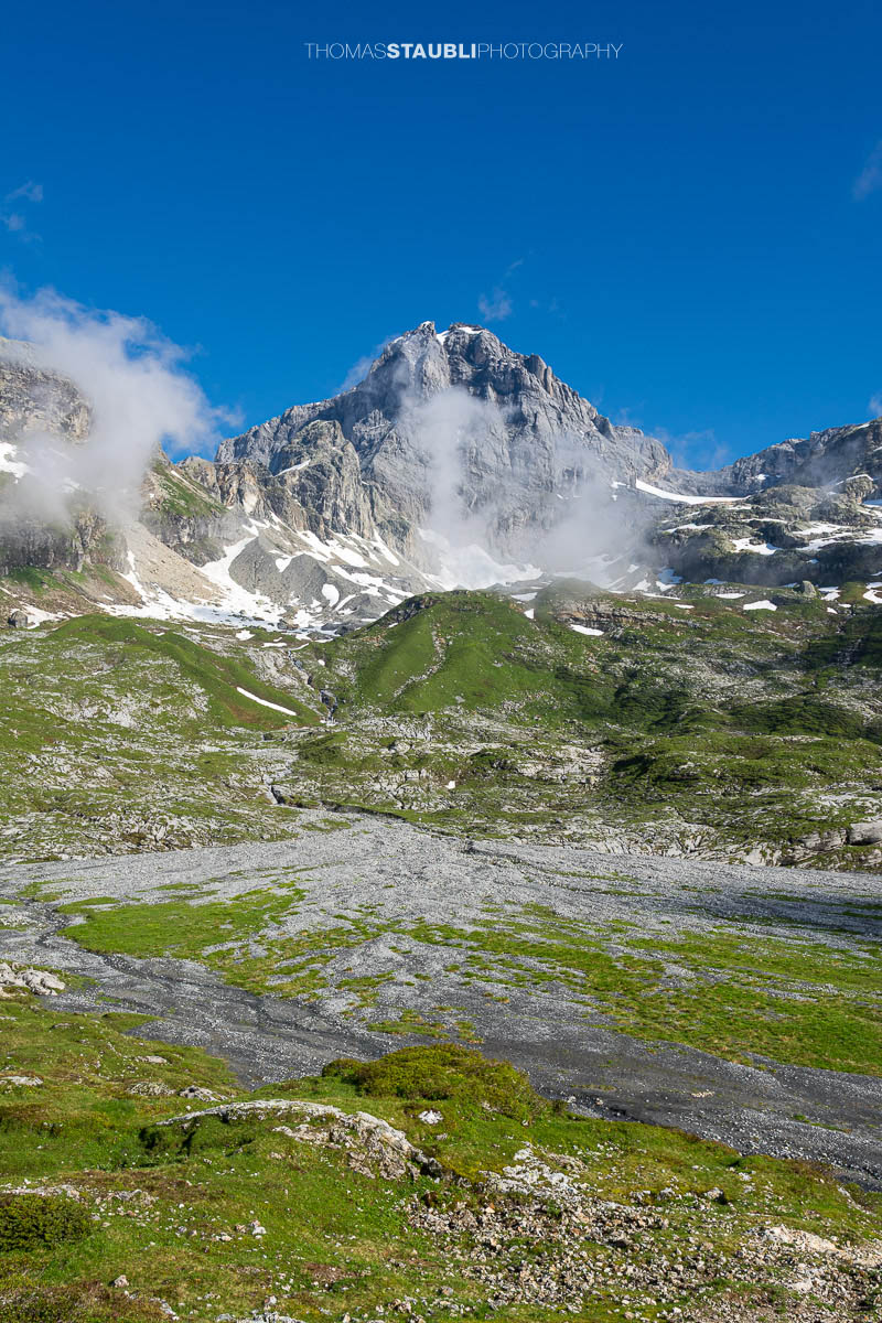 Blick zum Gross Windgällen im Maderanertal mit alpinen Wiesen, Schmelzwasserbach und aufziehenden Nebelschwaden.