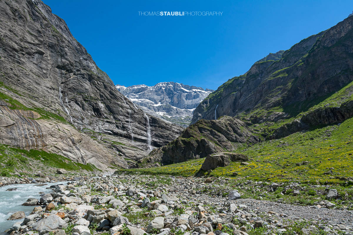 Der Chärstelenbach im Maderanertal fliesst zwischen Felsblöcken talwärts, während Wasserfälle über steile Felswände stürzen.