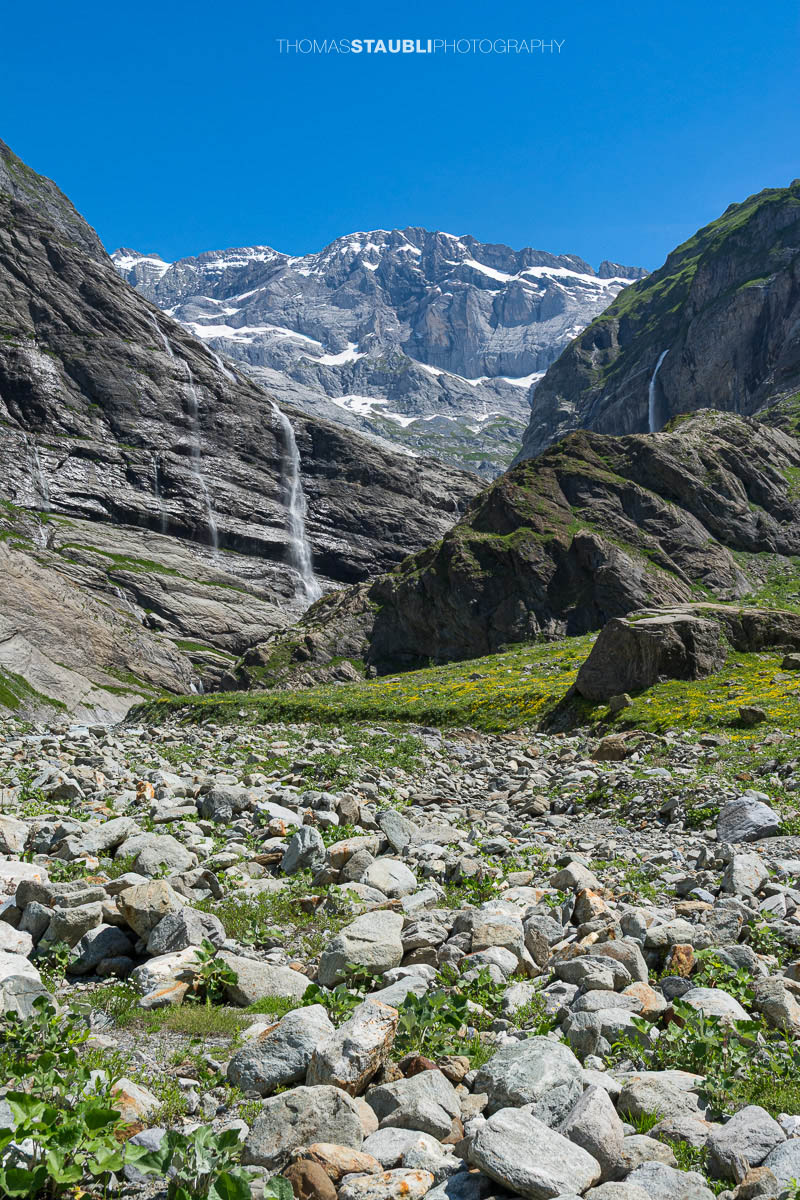 Der Chärstelenbach im Maderanertal fliesst zwischen Felsblöcken talwärts, während Wasserfälle über steile Felswände stürzen.