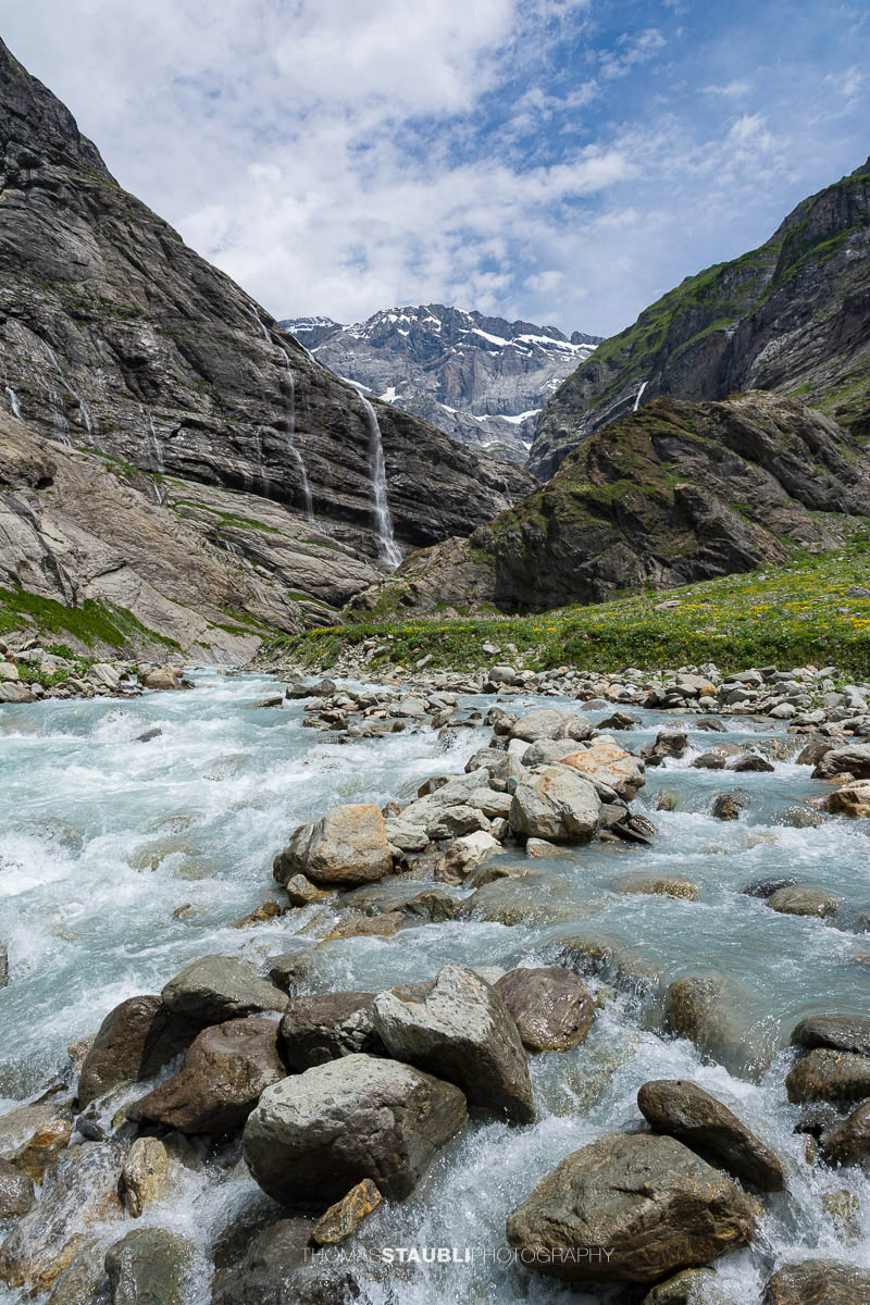 Der Chärstelenbach im Maderanertal fliesst zwischen Felsblöcken talwärts, während Wasserfälle über steile Felswände stürzen.