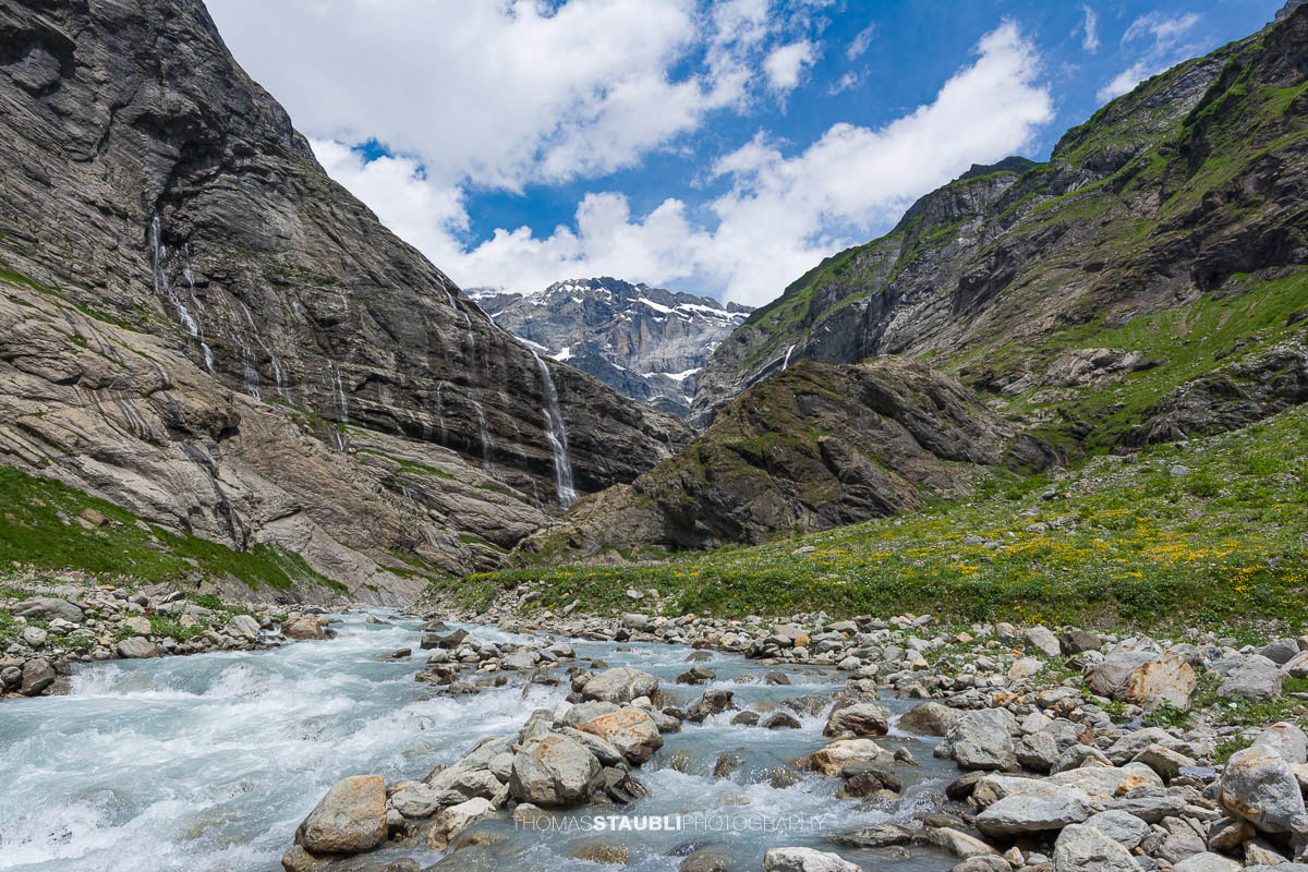 Der Chärstelenbach im Maderanertal fliesst zwischen Felsblöcken talwärts, während Wasserfälle über steile Felswände stürzen.