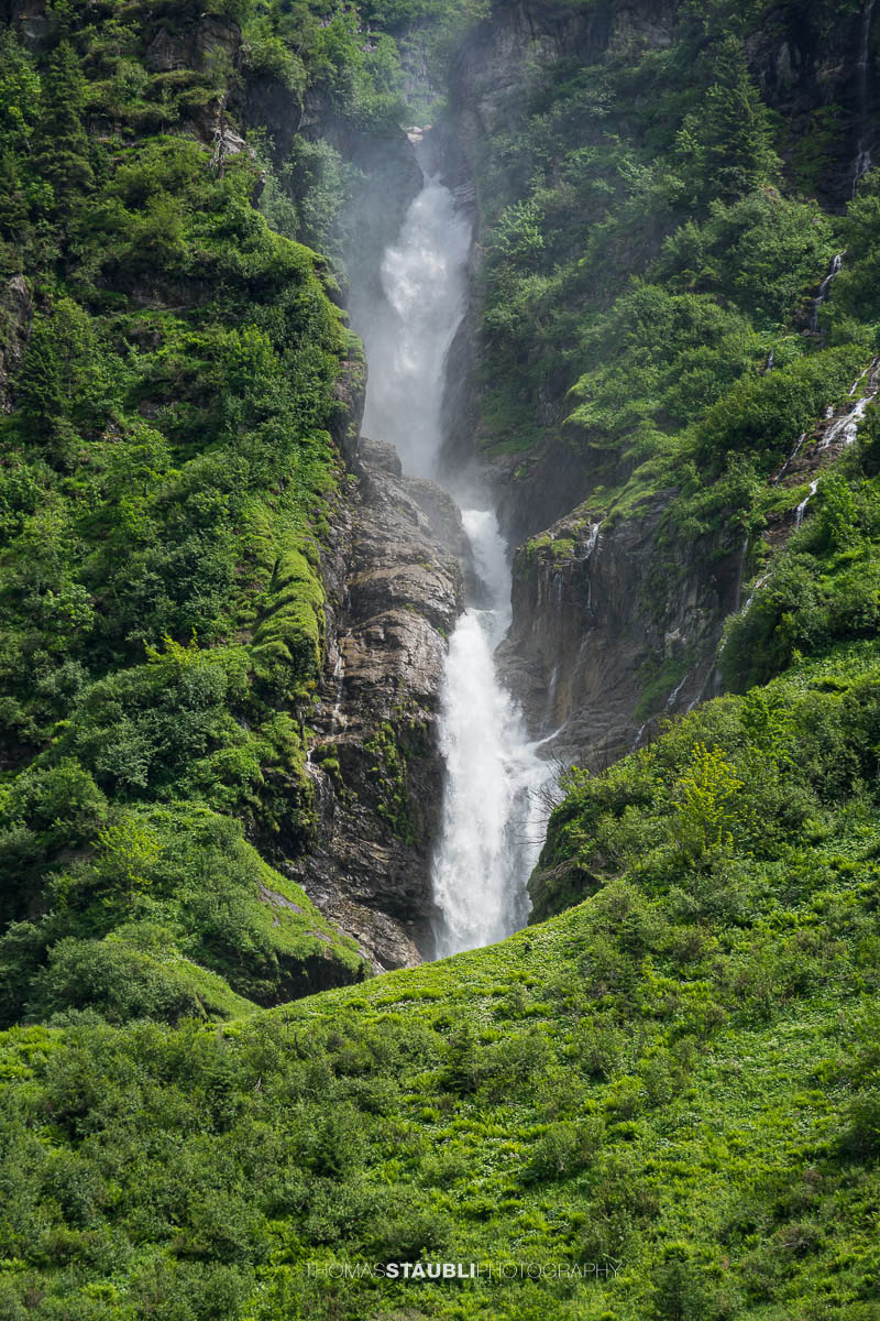 Der Stäuber Wasserfall im Maderanertal zwischen bewaldeten Berghängen und steilen Felswänden.