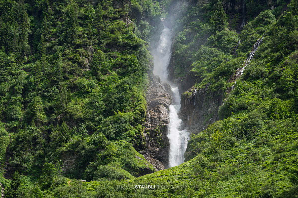 Der Stäuber Wasserfall im Maderanertal zwischen bewaldeten Berghängen und steilen Felswänden.