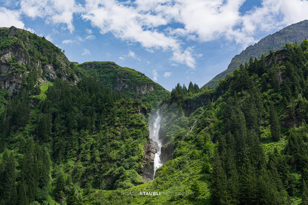 Der Stäuber Wasserfall im Maderanertal zwischen bewaldeten Berghängen und steilen Felswänden.