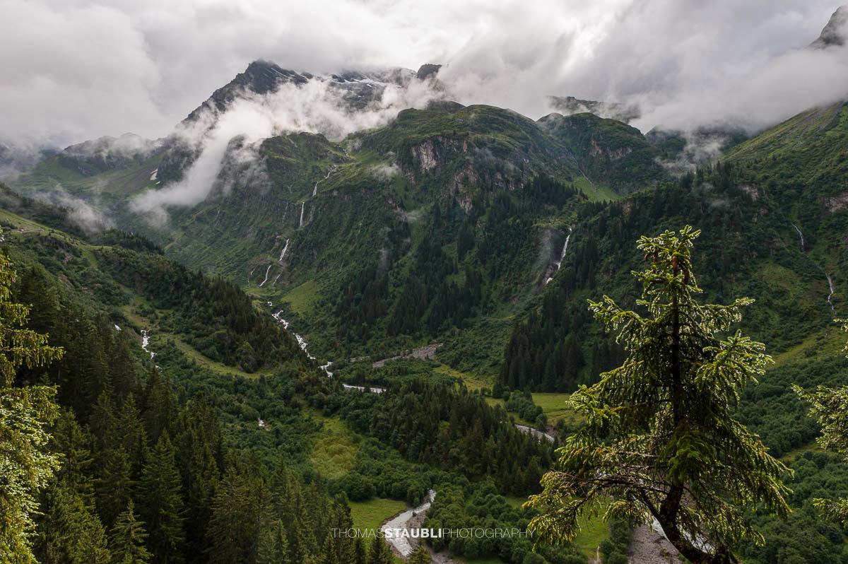 Blick ins hintere wildromantisches Maderanertal mit tief hängenden Wolken und bewaldeten Berghängen.