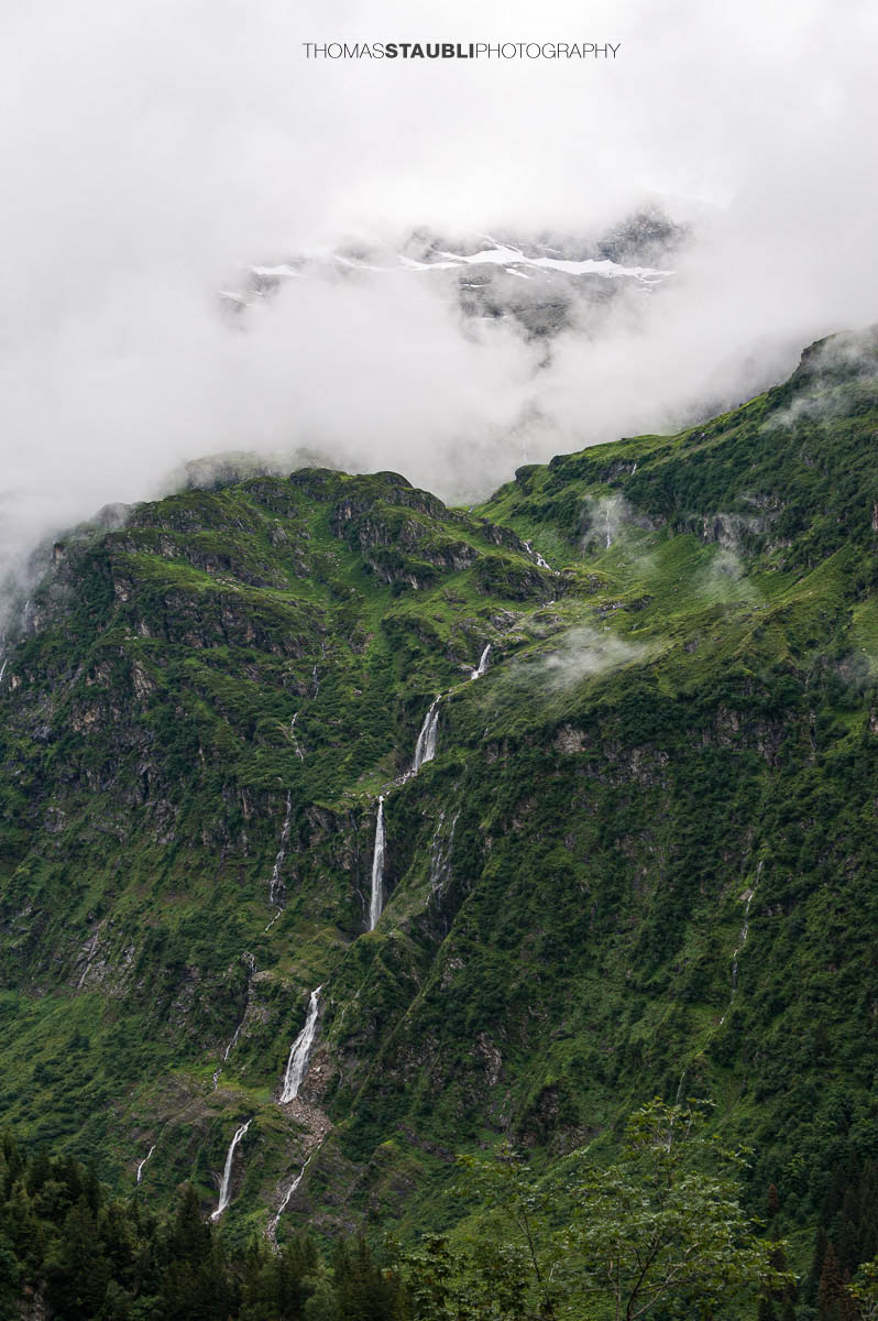 Wasserfall im Maderanertal mit tief hängenden Wolken und bewaldeten Berghängen.