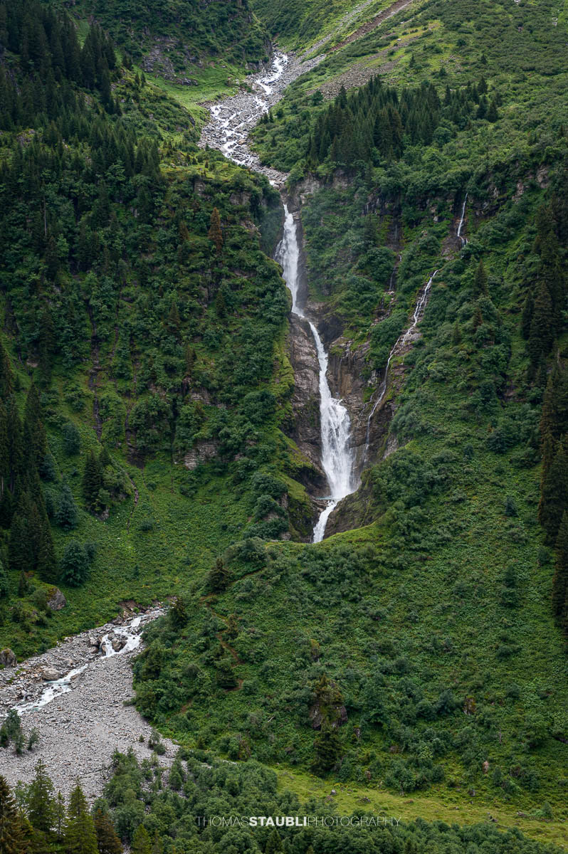 Der Stäuber Wasserfall stürzt zwischen bewaldeten Hängen im Maderanertal ins Tal.