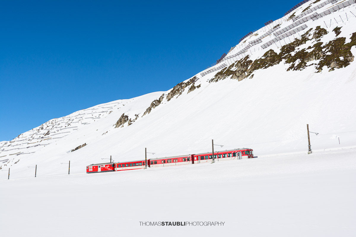 Matterhorn Gotthard Bahn fährt durch die verschneite Landschaft am Oberalppass.