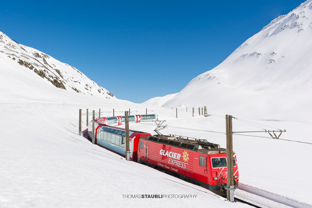 Glacier Express fährt durch die verschneite Landschaft am Oberalppass.