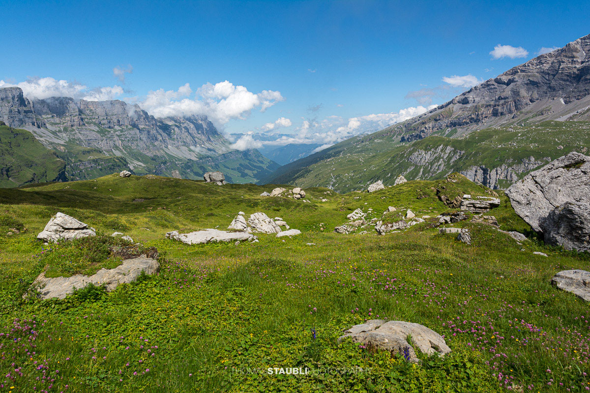 Blick vom Griessbödemli hinunter in die alpine Landschaft des Urnerbodens mit Wolken und grünen Bergweiden.