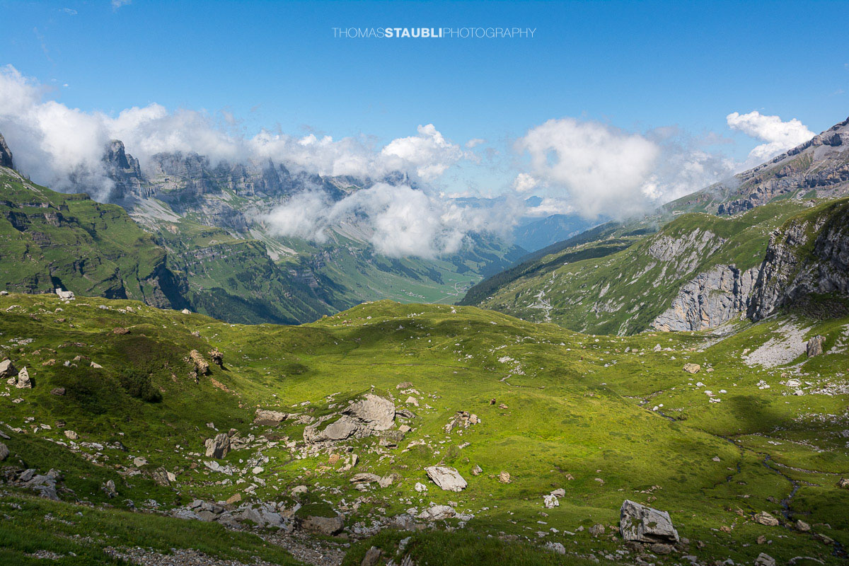 Blick vom Griessbödemli hinunter in die alpine Landschaft des Urnerbodens mit Wolken und grünen Bergweiden.