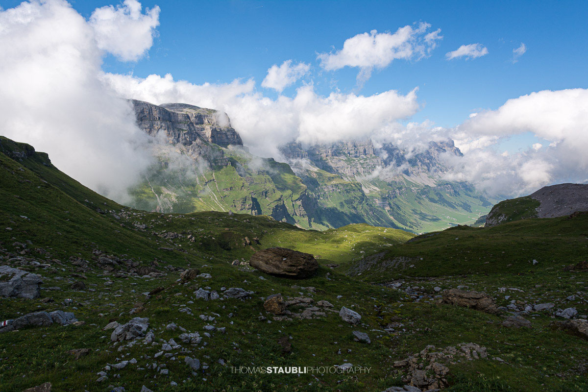 Blick vom Griessbödemli hinunter in die alpine Landschaft des Urnerbodens mit Wolken und grünen Bergweiden.