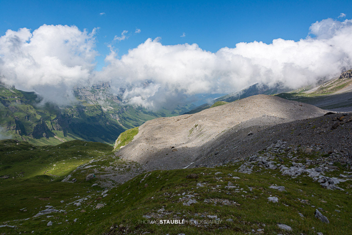 Blick vom Griessbödemli hinunter in die alpine Landschaft des Urnerbodens mit Wolken und grünen Bergweiden.