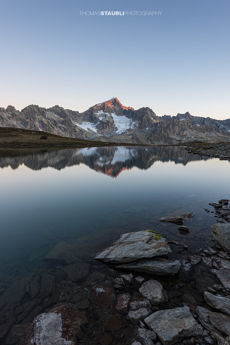 Die ersten Sonnenstrahlen treffen den Galenstock und spiegeln sich im Unteren Schwärziseeli bei den Stotzigen Firsten.